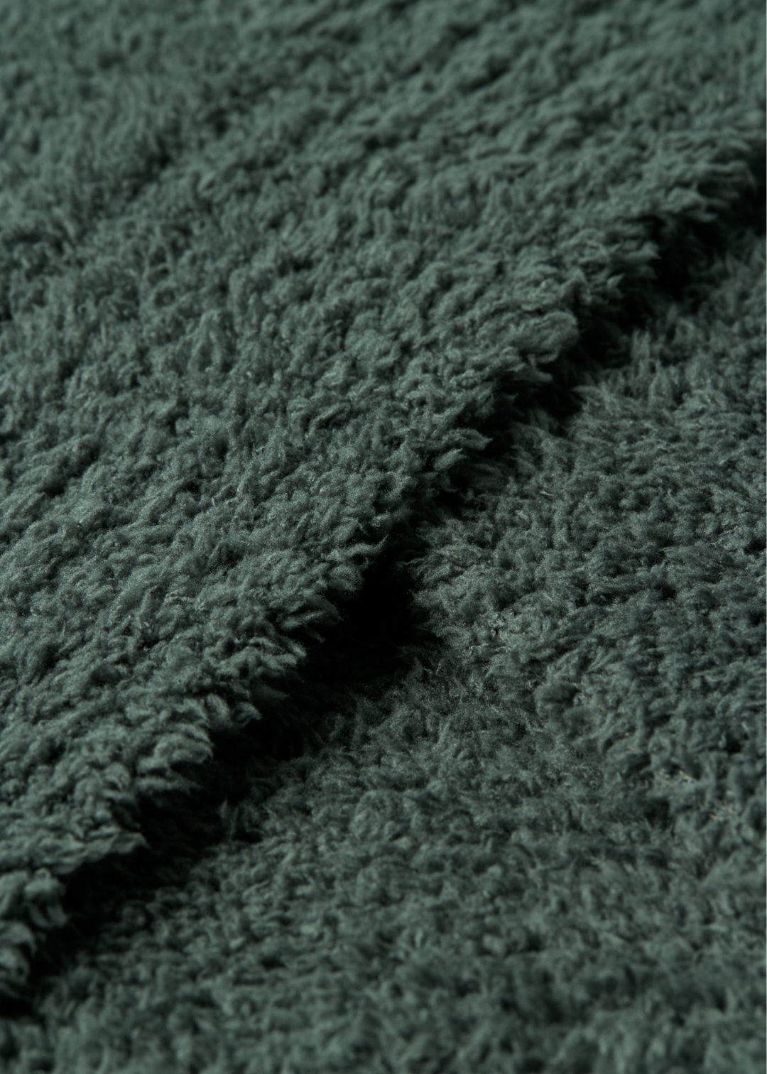 A close-up of a dark green, plush, textured fabric with a soft, looped pile and a folded edge showing the depth of the material.