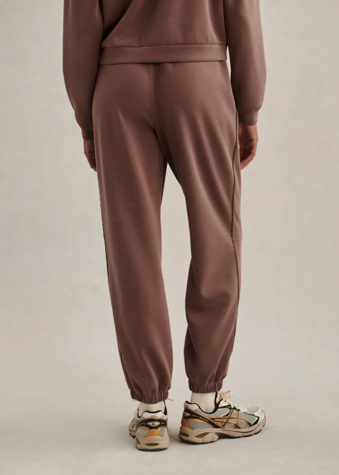Woman wearing a brown colored matching sweat set and turned facing backwards.