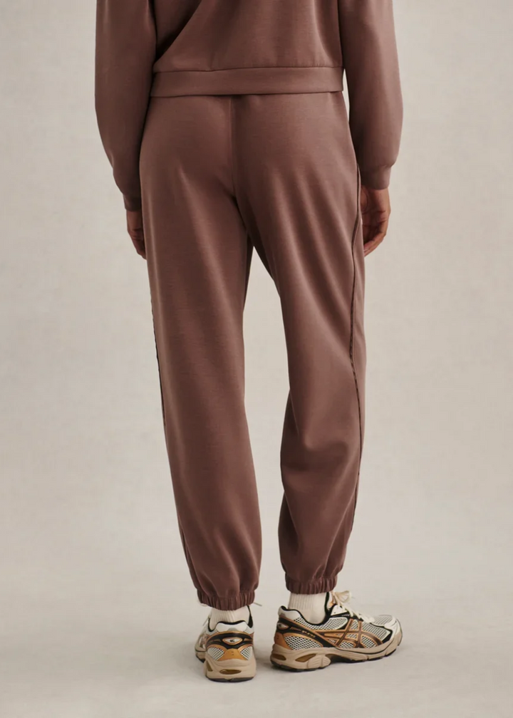 Woman wearing a brown colored matching sweat set and turned facing backwards.