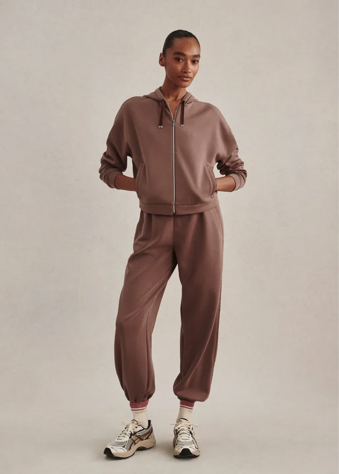 Woman wearing a brown colored matching sweat set with hands in her pockets.
