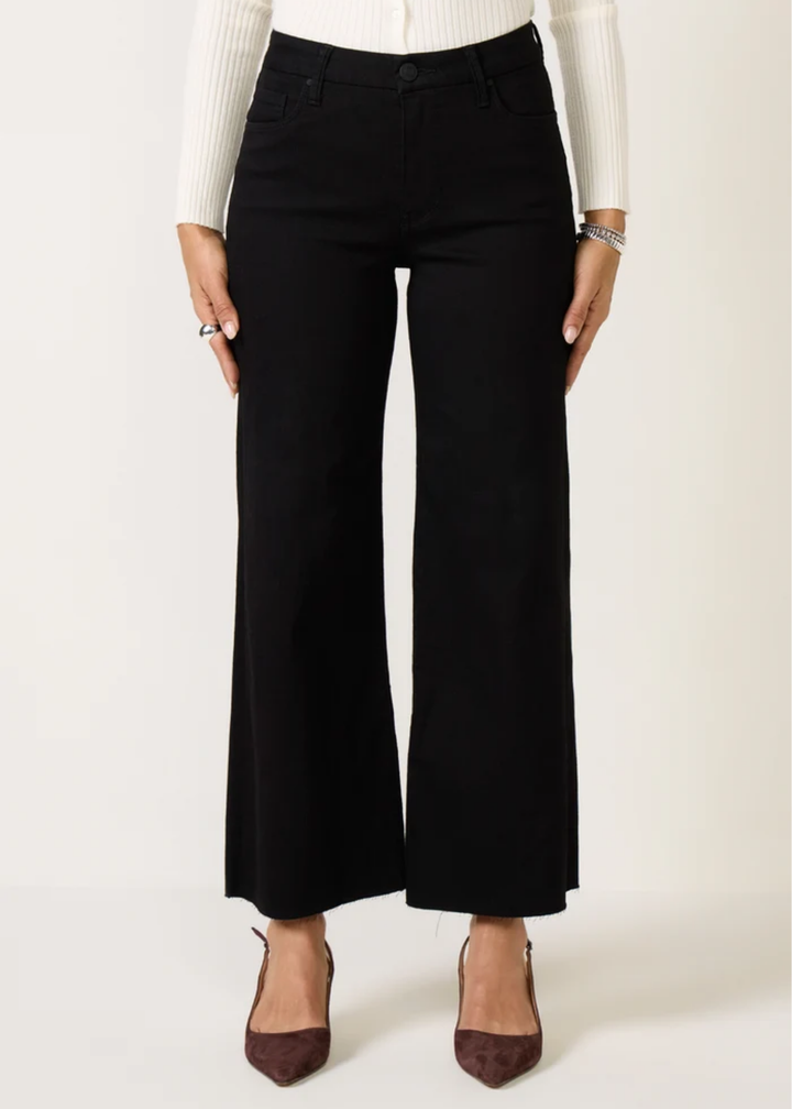 A model wearing black wide-leg cropped pants, styled with a white ribbed long-sleeve top and dark brown pointed-toe heels against a plain off-white studio background.