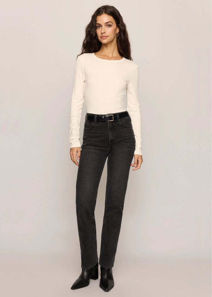 A woman modeling a cream long-sleeve crewneck top and black high-waisted straight-leg jeans with a black belt, paired with black ankle boots, against a light gray studio background.