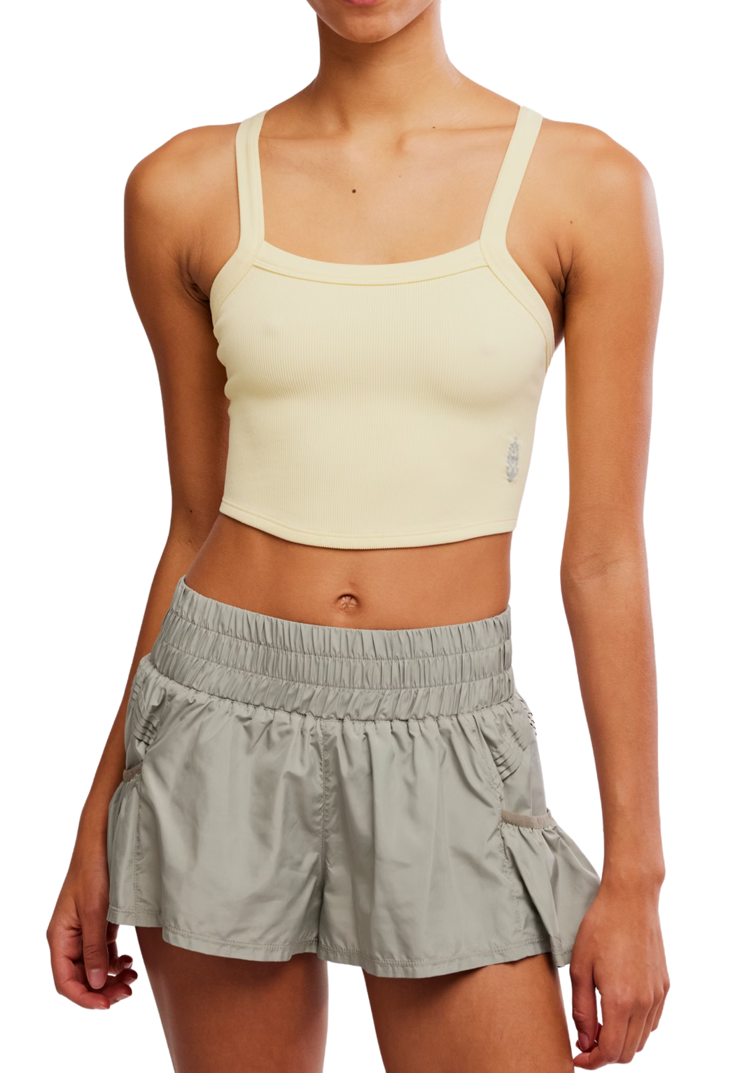 Woman wearing a light yellow sports bra and gray shorts on a white background