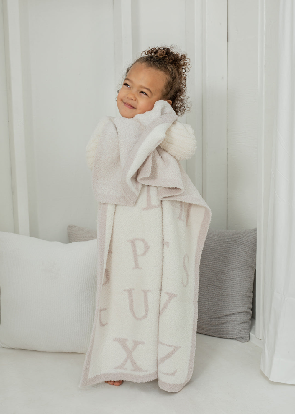 Girl holding a cream and brown blanket with an ABC pattern