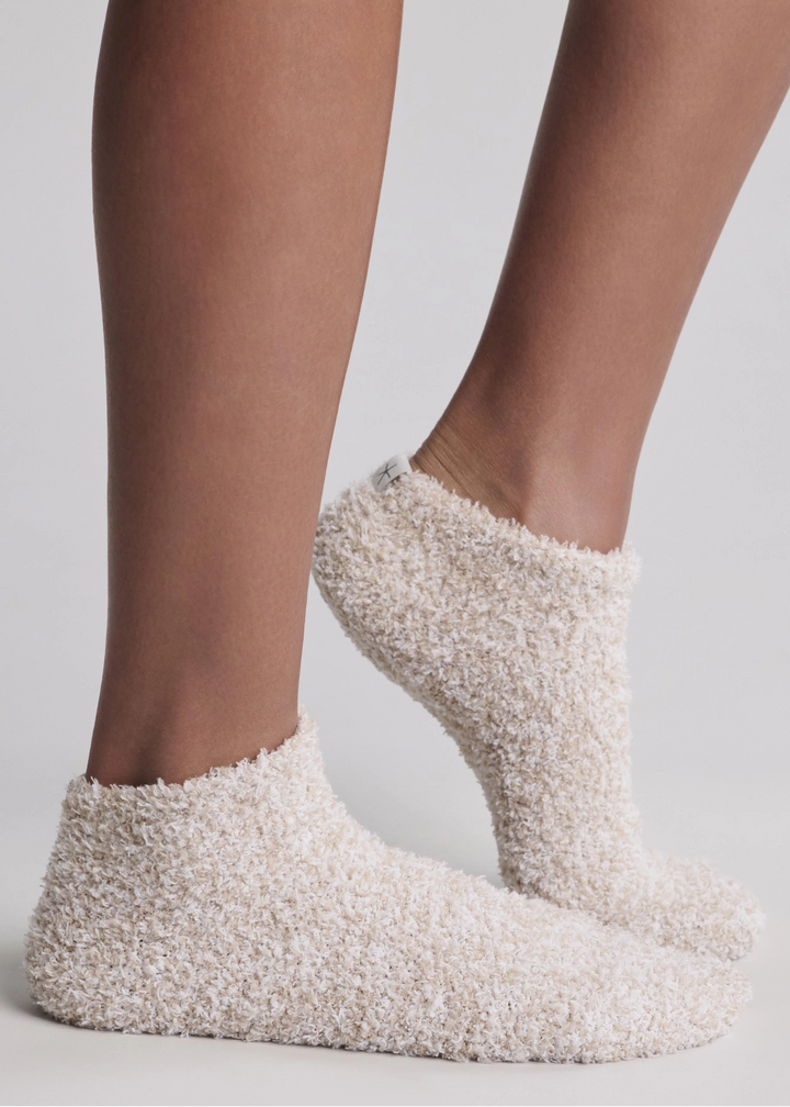Close up of a woman wearing tan ankle socks and standing in front of a white background
