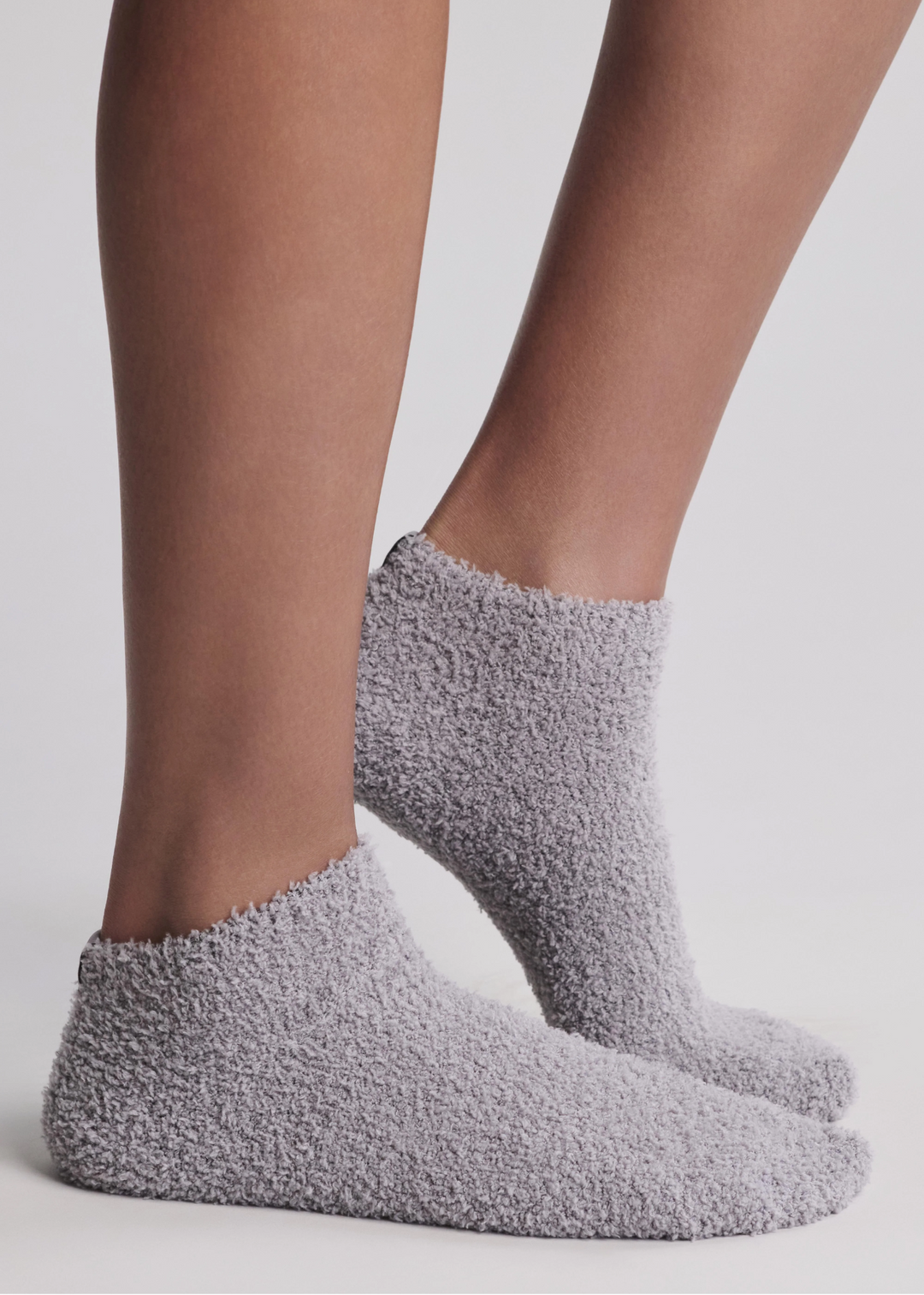 Close up of a woman wearing grey ankle socks standing in front of a white background