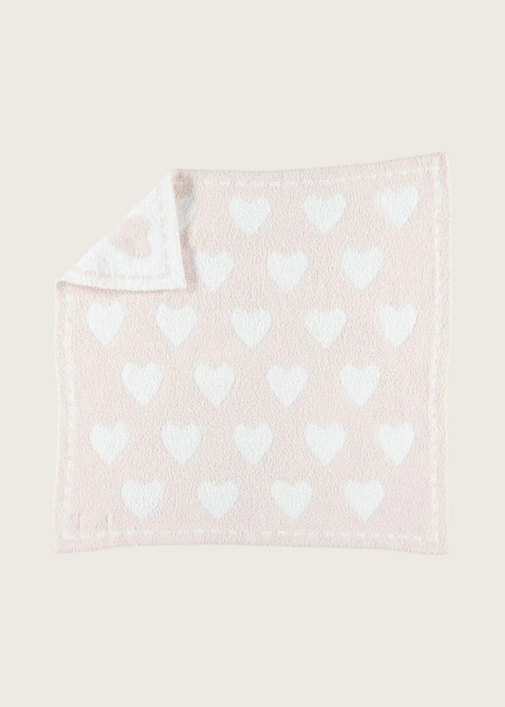 A reversible pink blanket with white hearts on a white background