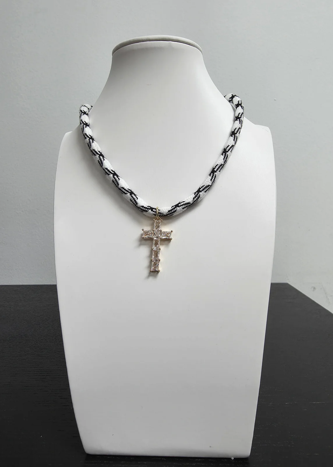 Black and white paracord necklace with a gold and CZ cross on a white display