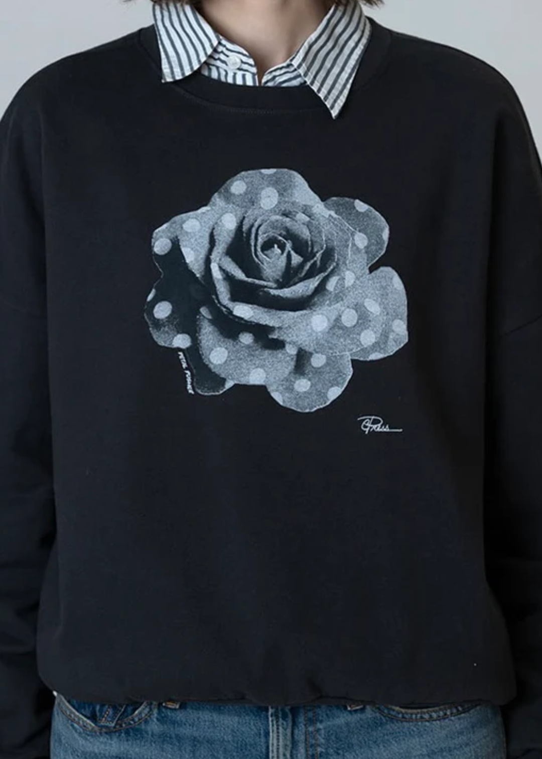 Woman wearing a black sweatshirt with a black and white polka dot rose graphic over a black and white striped button down