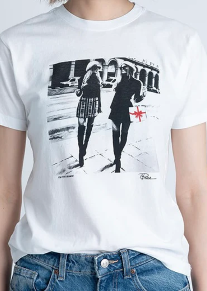 Woman wearing a white graphic tee with a black and white city street graphic with jeans in front of a grey background