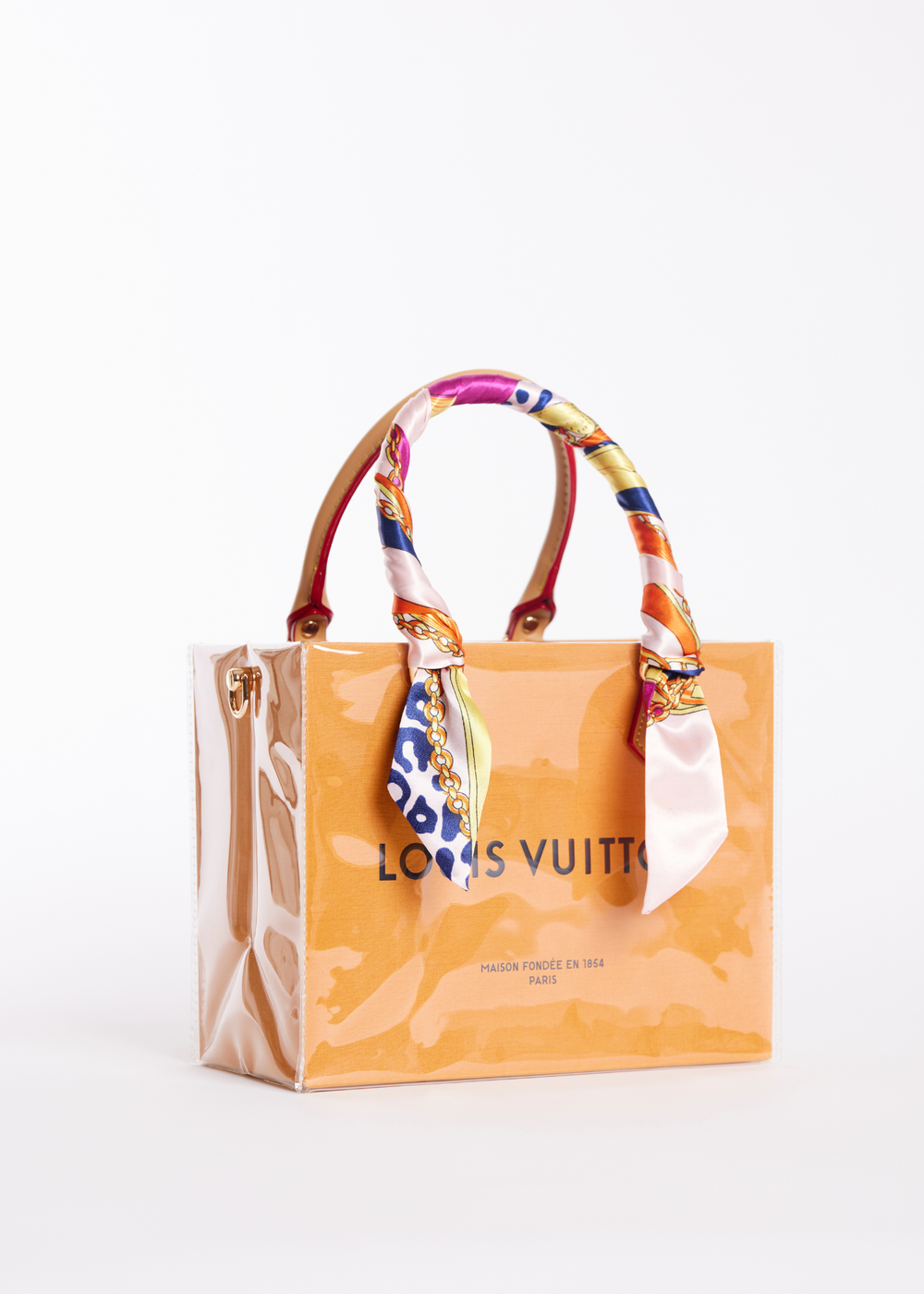 Small clear coated Louis Vuitton shopping bag with a multicolor scarf handle against a white background