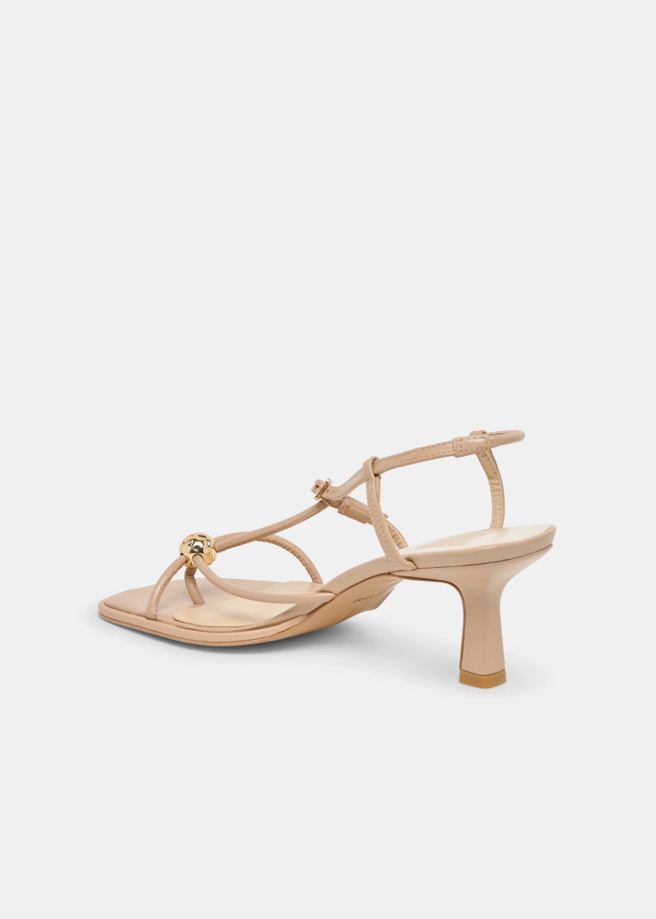 Side view of tan strappy heels with a gold button against a white background