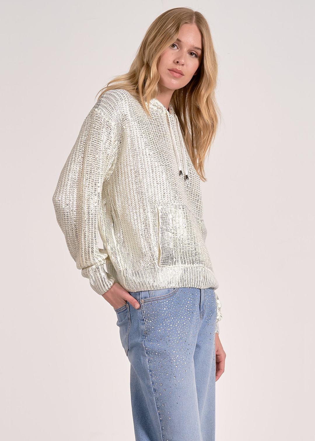 Woman turned to the side wearing a white sequin hoodie with jeans against a white background