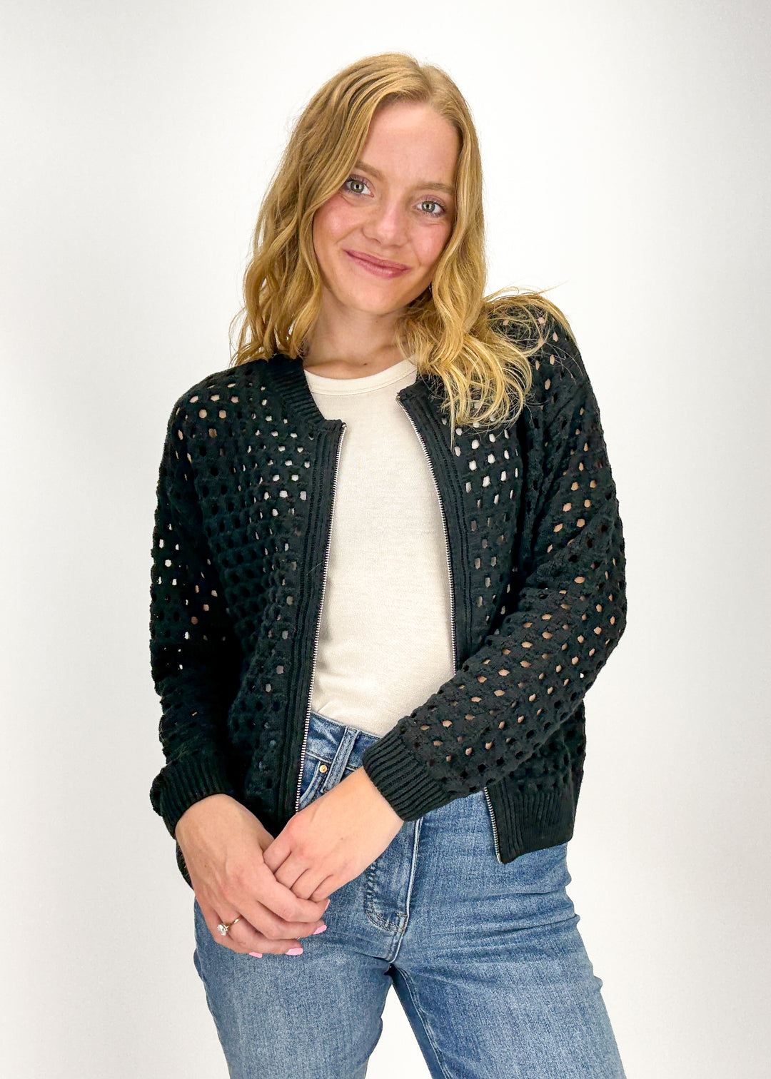 woman wearing black crochet zip up cardigan over cream tank with blue denim jeans