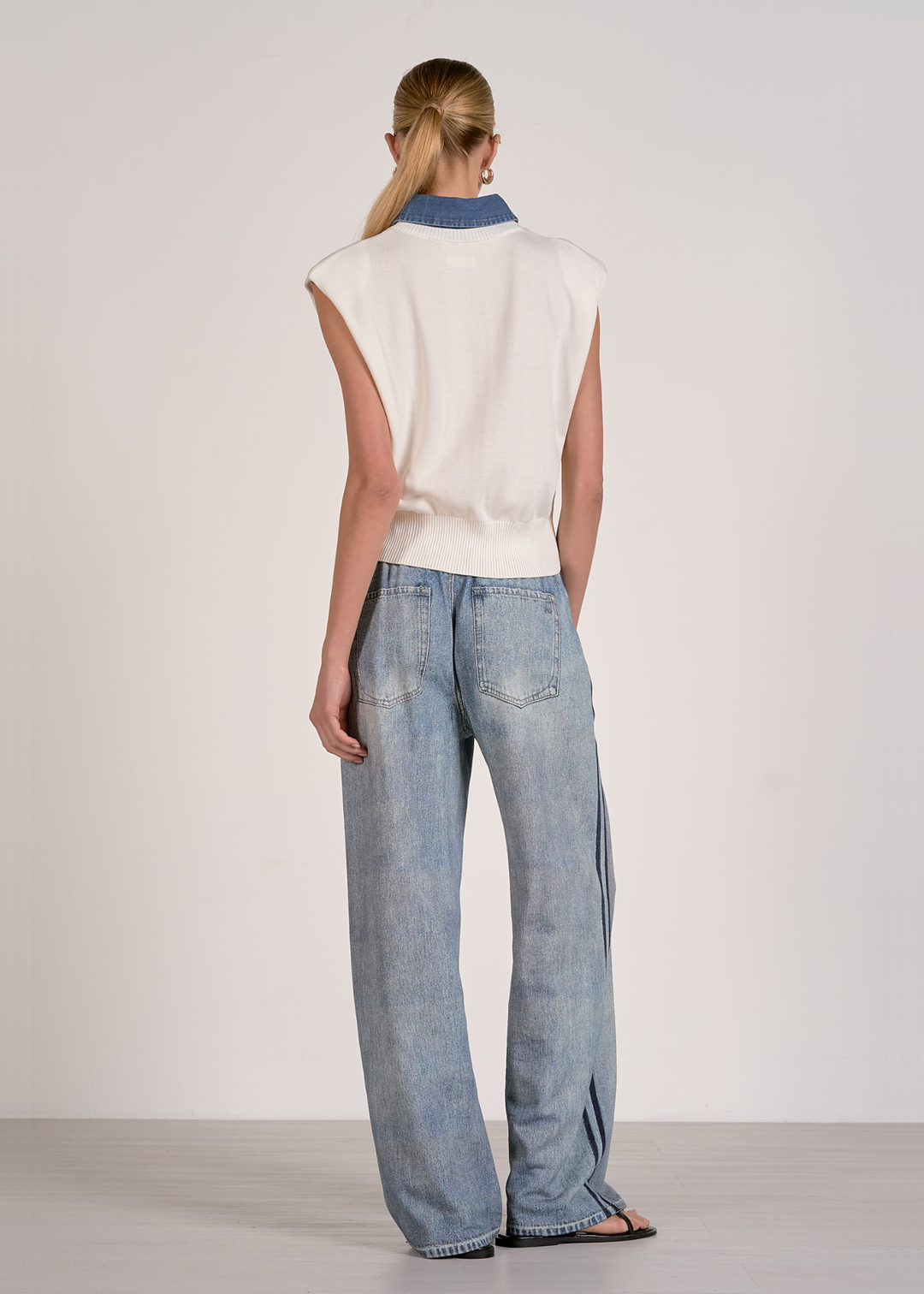 Woman turned around wearing a white knit top with jeans