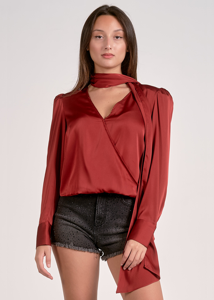 Woman wearing a rust colored top with a v-neck and scarf