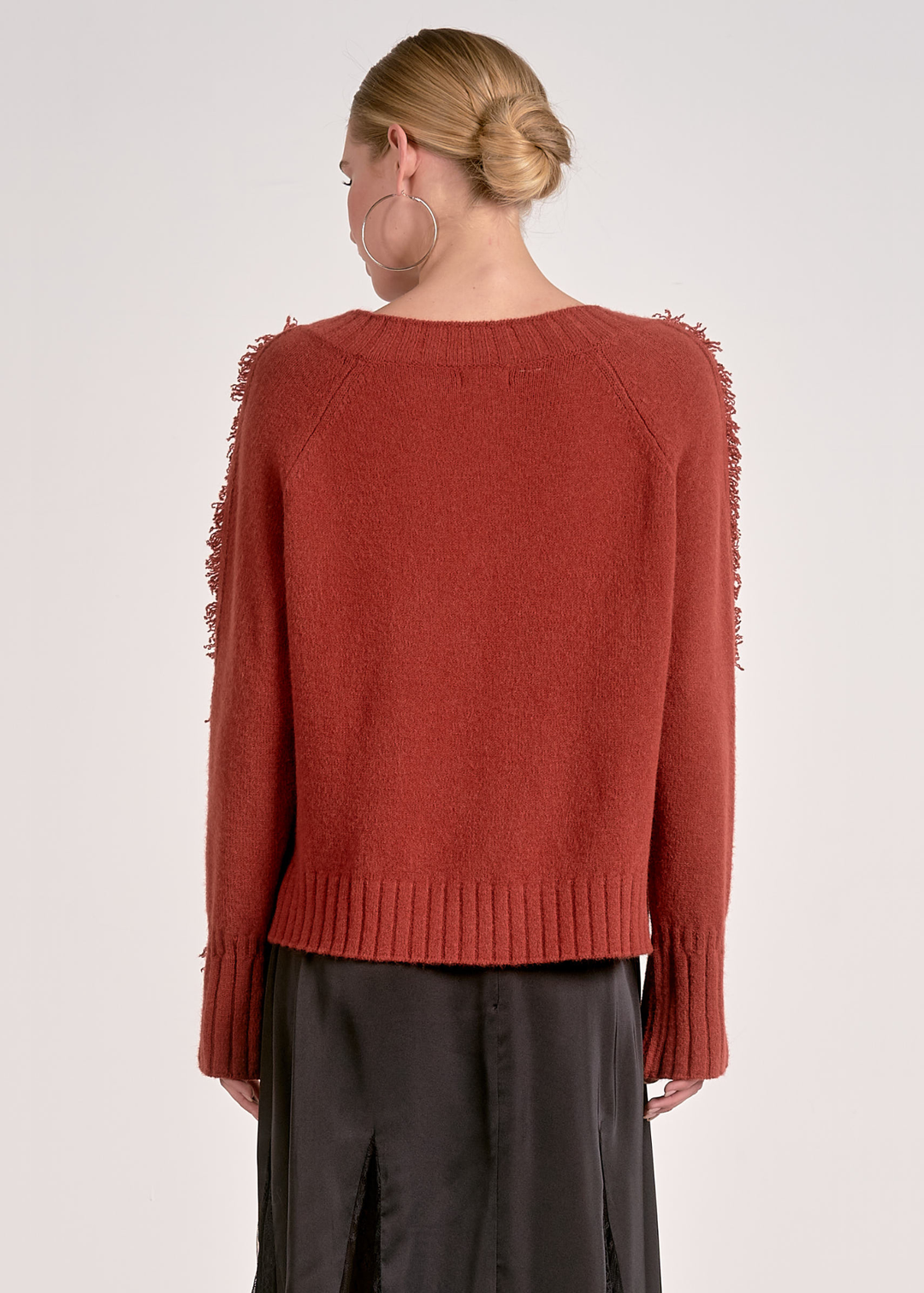 Woman turned around wearing a v-neck rust colored sweater against a white background