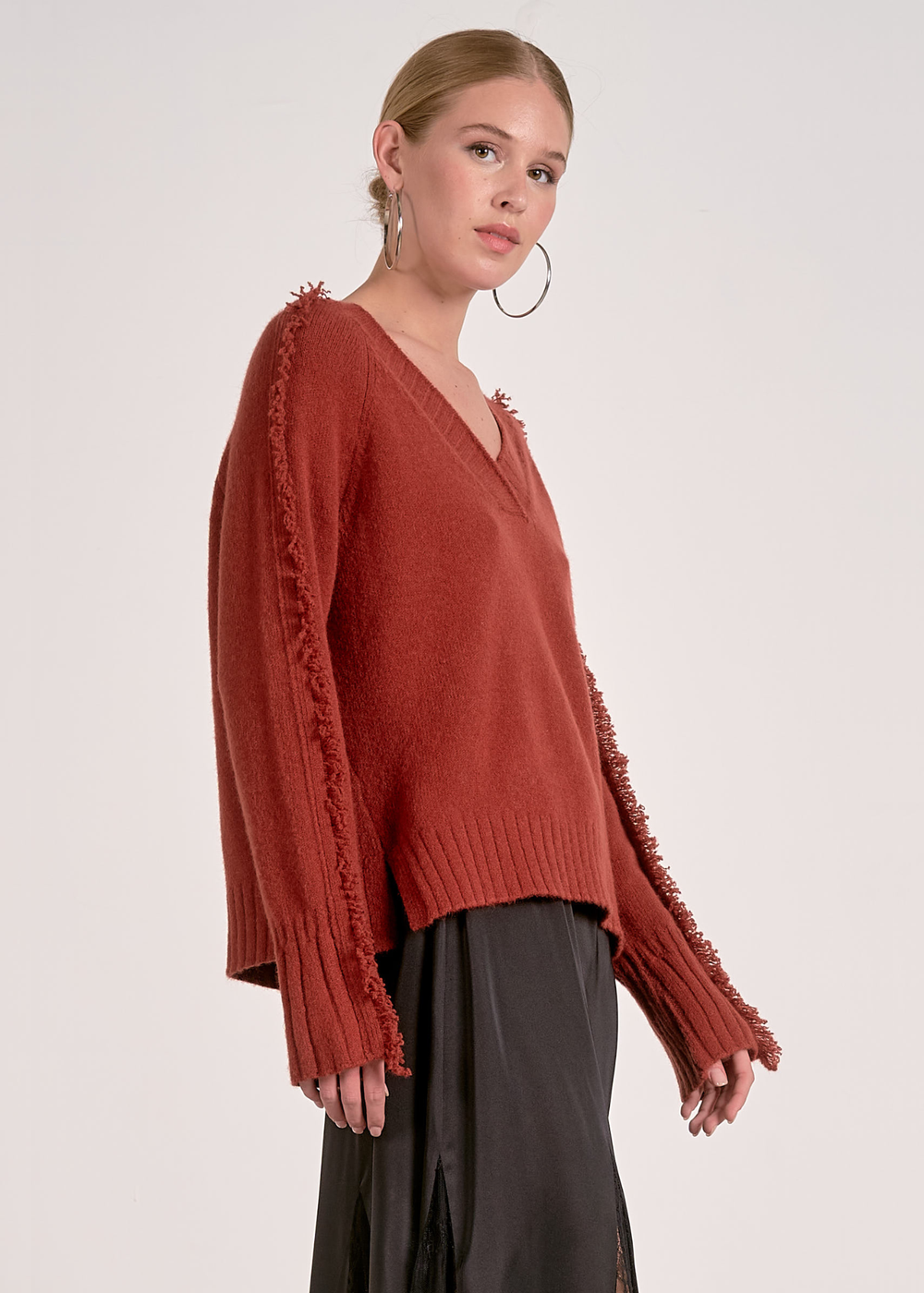 Woman turned to the side wearing a v-neck rust colored sweater against a white background