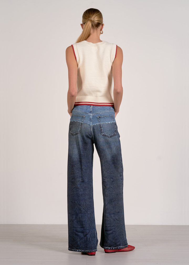 Woman turned around wearing a white sleeveless knit top with red striped trim and jeans