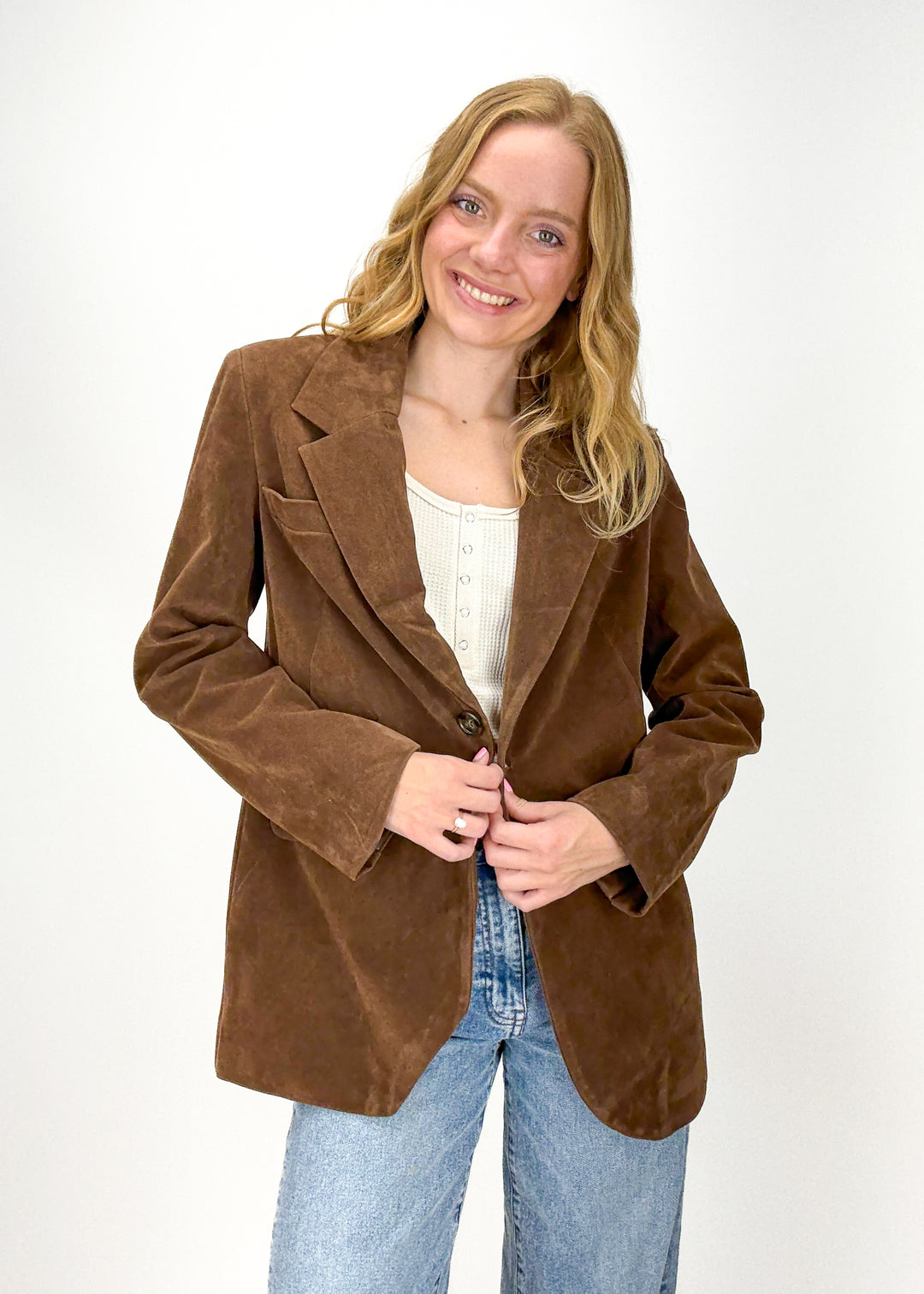 woman wearing brown faux suede blazer over cream waffle knit henley with light wash denim jeans
