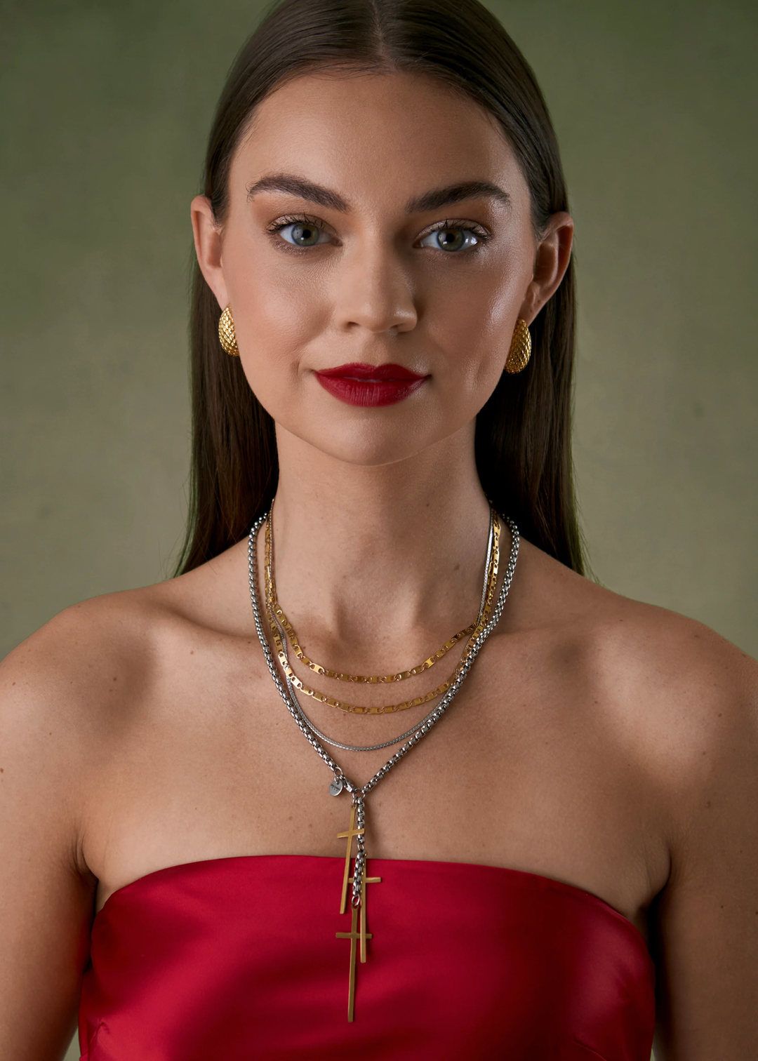 Woman wearing multiple necklaces including a silver chain necklace with three gold cross charms
