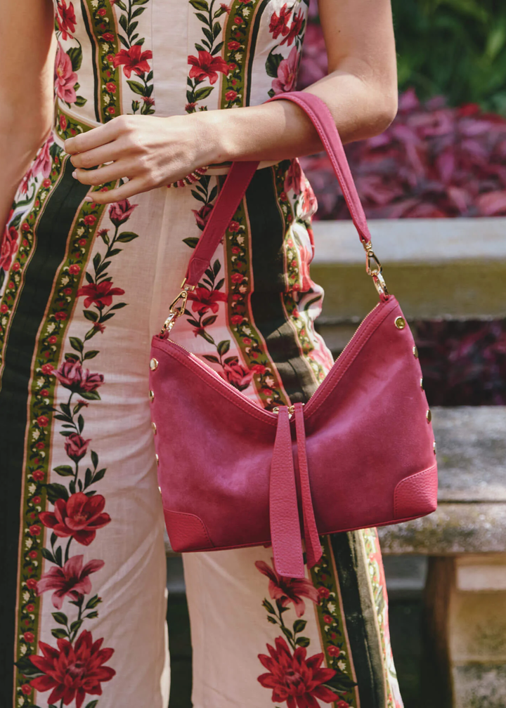 Woman holding a fuschia suede and leather handbag with gold accents