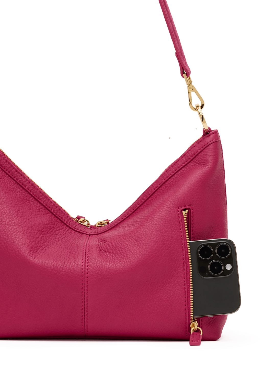 Fuschia suede and leather handbag with gold accents and a phone in the pocket against a white background