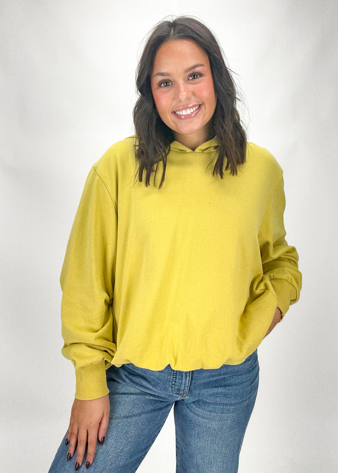 Woman wearing a yellow hoodie and blue jeans on a white background