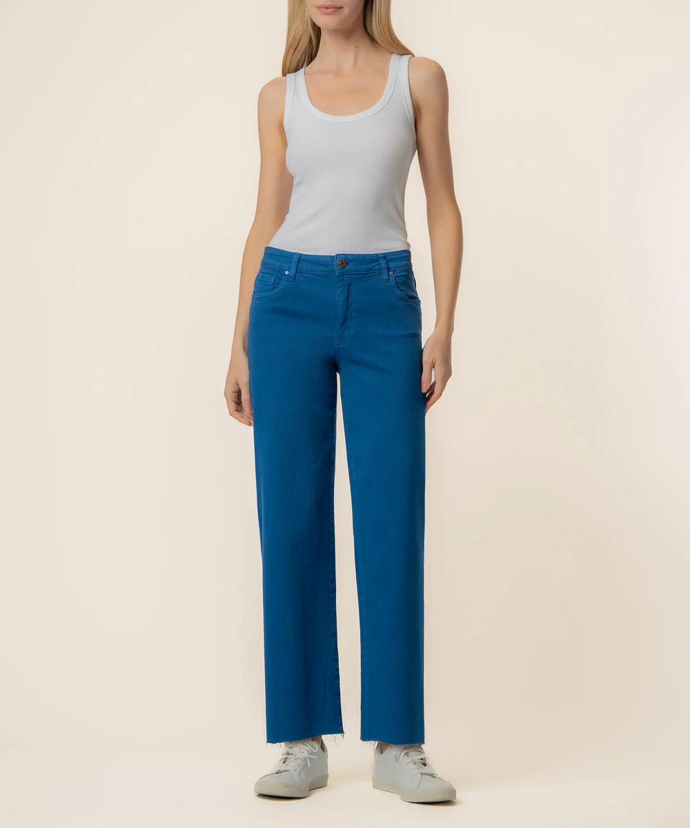Woman wearing blue denim pants and a white tank top on a beige background