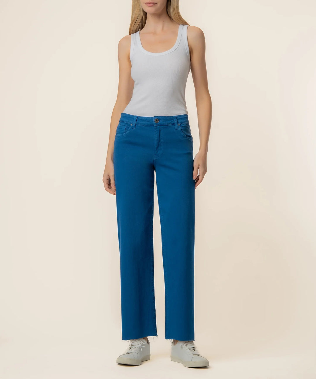 Woman wearing blue denim pants and a white tank top on a beige background