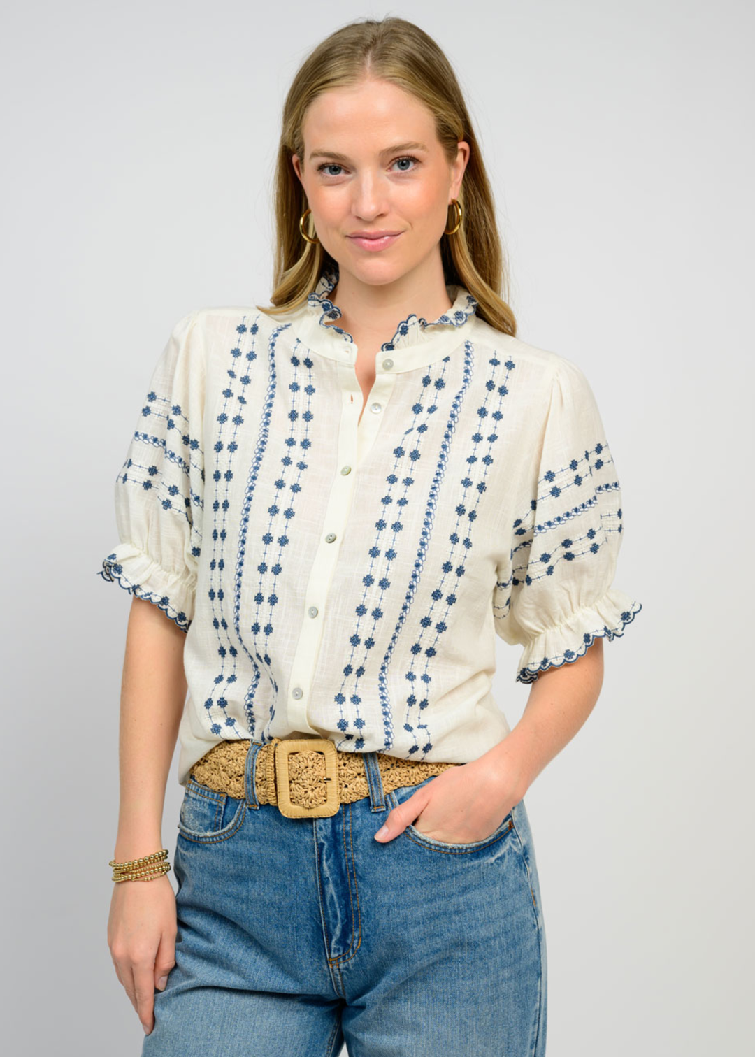 Woman wearing an ivory puff sleeve top with blue embroidery and jeans