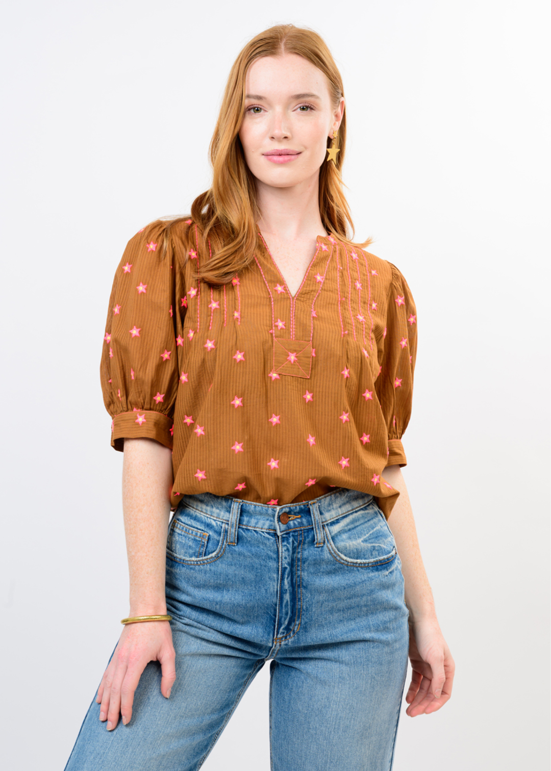 Woman wearing a rust colored top with a pink pattern and jeans