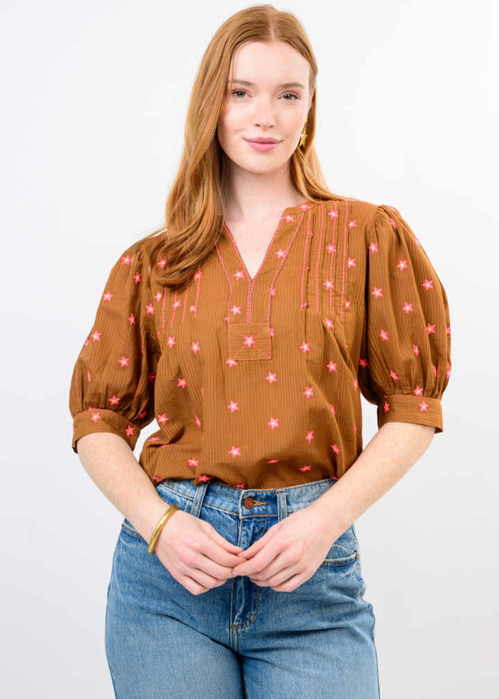 Woman wearing a rust colored top with a pink pattern and jeans