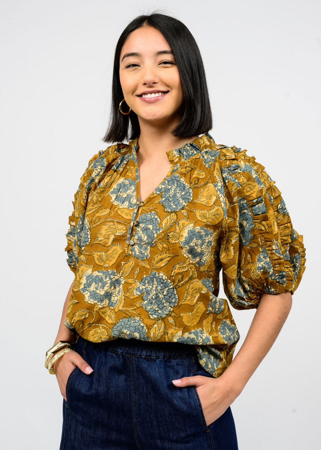Woman wearing a copper colored top with a yellow and blue floral hydrangea print and a v neckline