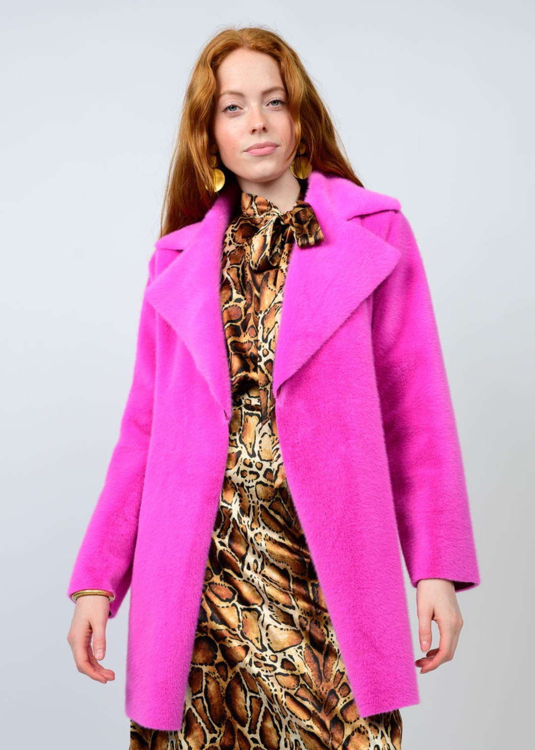 Woman wearing a pink coat with a brown patterned dress against a white background