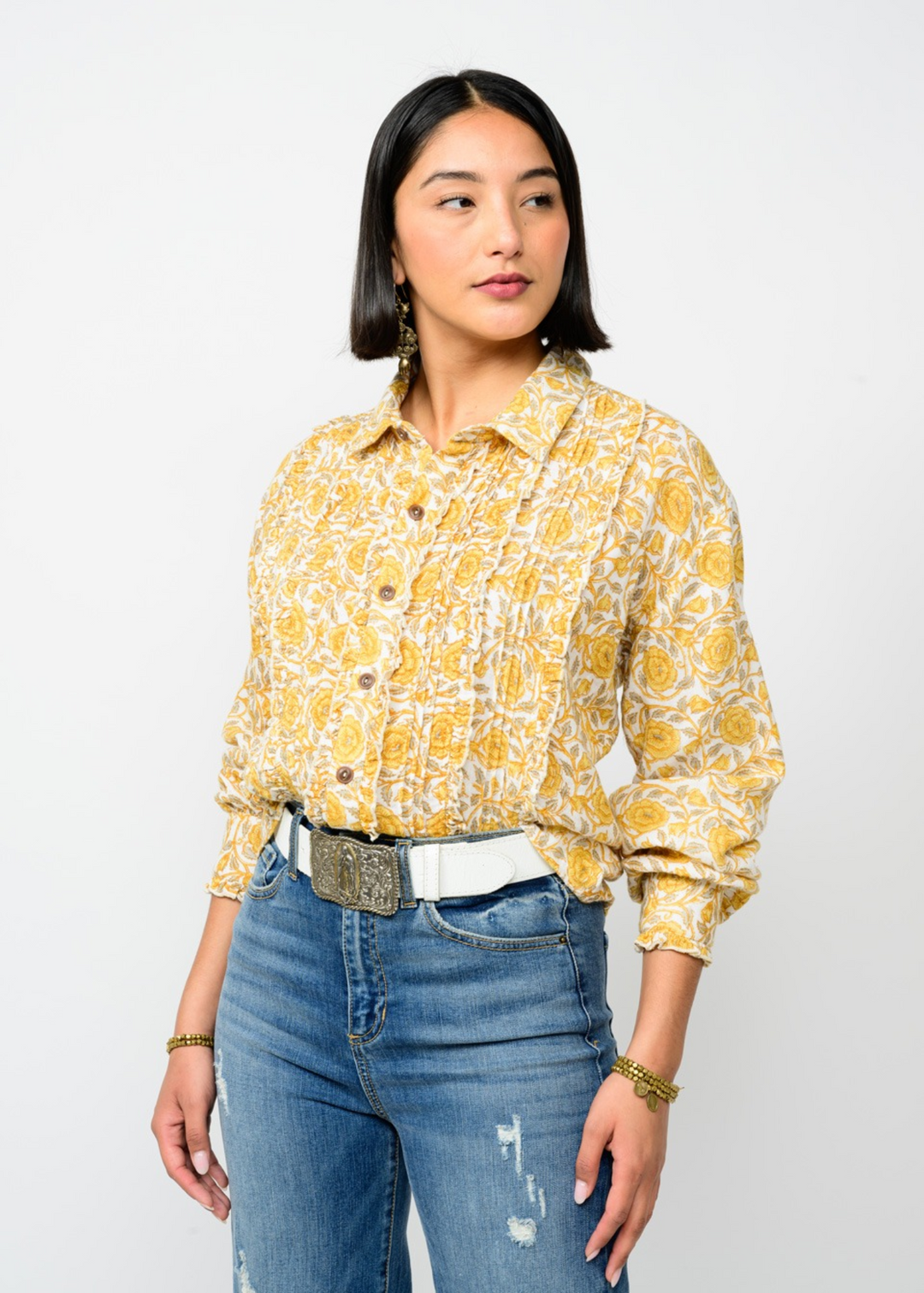 Woman wearing a gold button down top with a floral print and a collared neckline