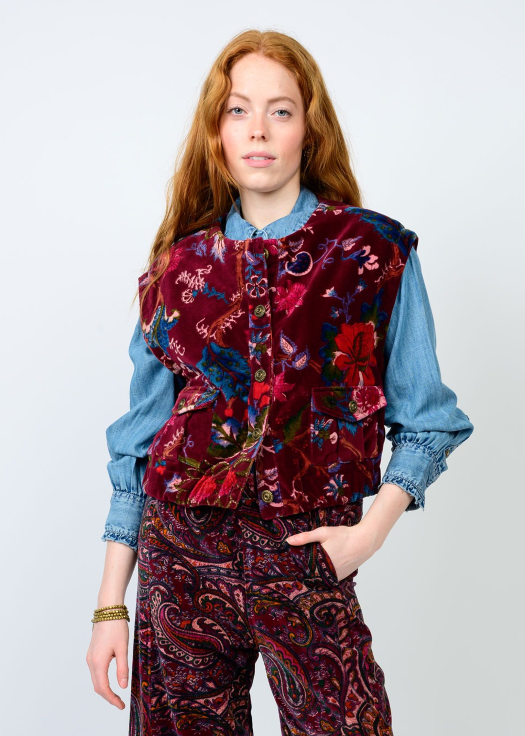 Woman with hand in pocket wearing a maroon floral vest against a white background