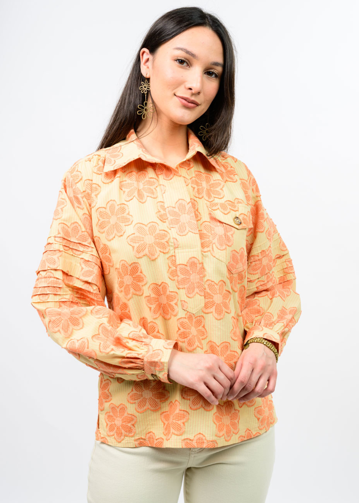 Woman wearing an orange and yellow floral collared top with tan pants