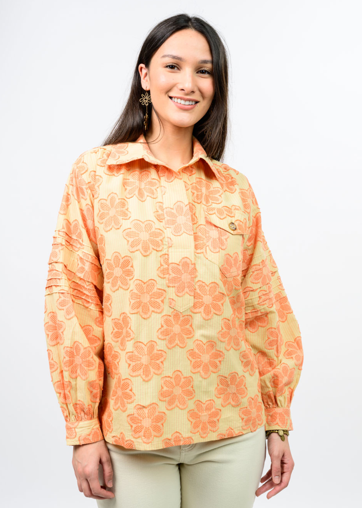 Woman wearing an orange and yellow floral collared top with tan pants