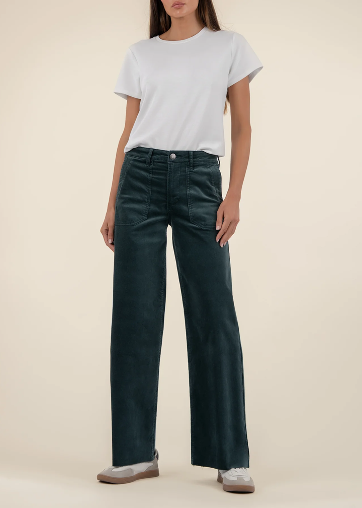 Woman wearing teal velvet jeans with a white t-shirt and sneakers against a tan background