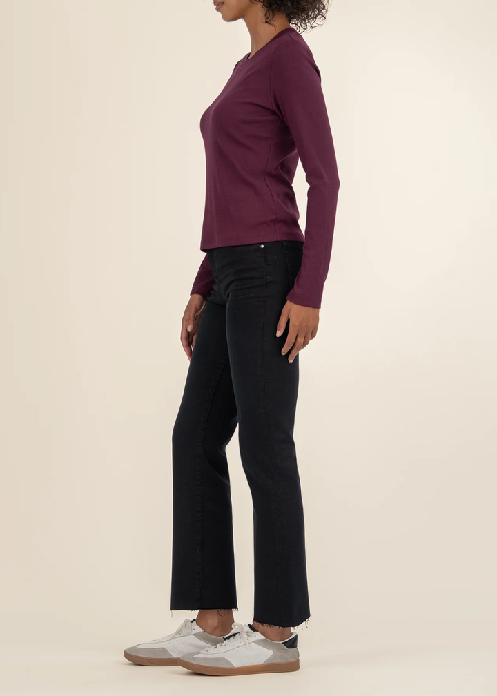 Woman turned to the side wearing a maroon long sleeve tee with black jeans and white sneakers in front of a white background