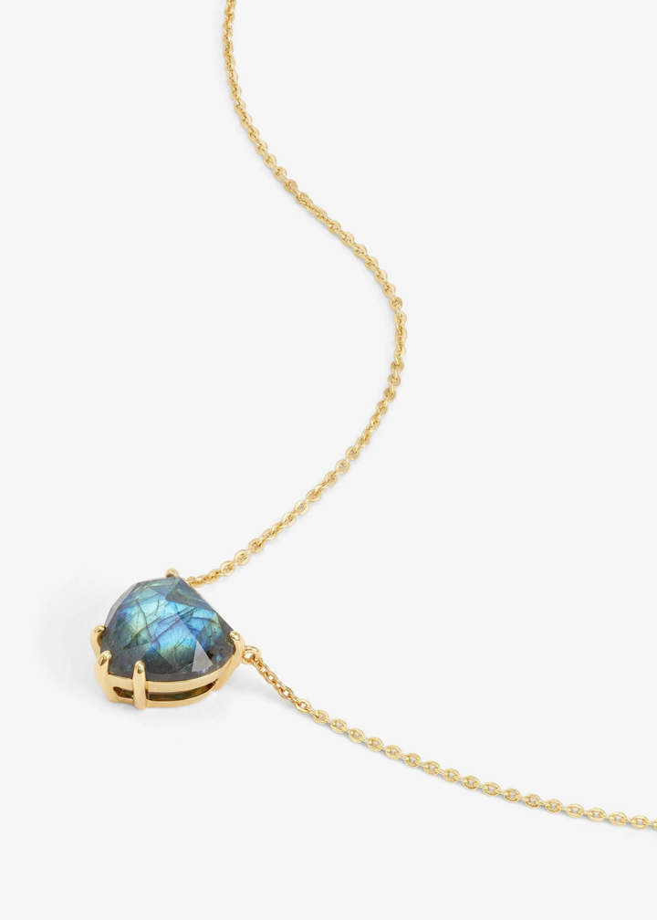 Heart shaped labradorite pendant on a gold chain necklace laying on a white background