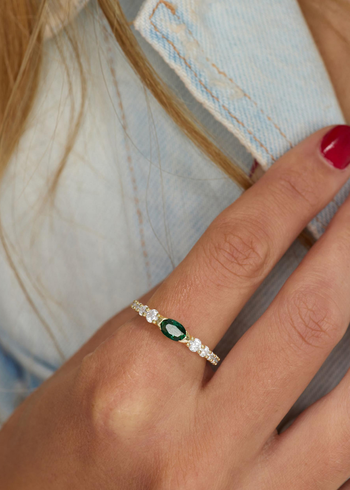 Woman wearing a gold ring with simulated diamonds and an emerald stone 