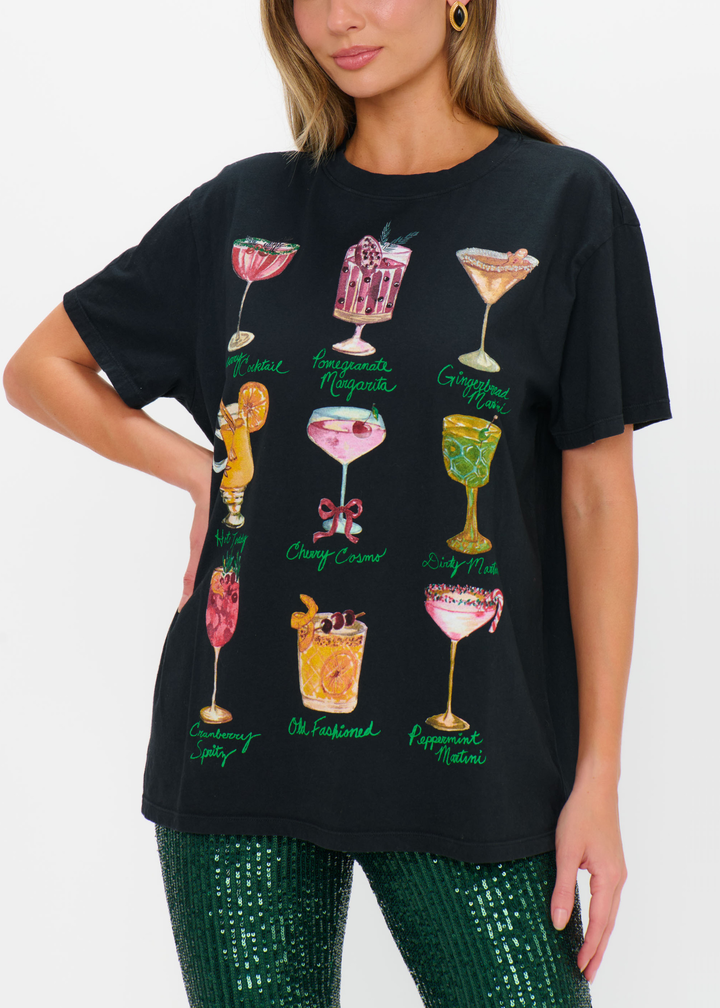Woman with a hand on hip wearing a black cocktails graphic tee with green sequin pants against a white background
