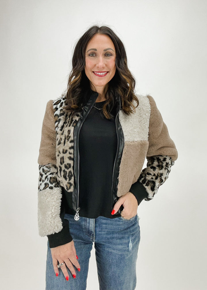 A woman wearing a patchwork jacket featuring faux fur, leather details, and leopard print accents, styled with a black top and jeans for a bold and trendy look.