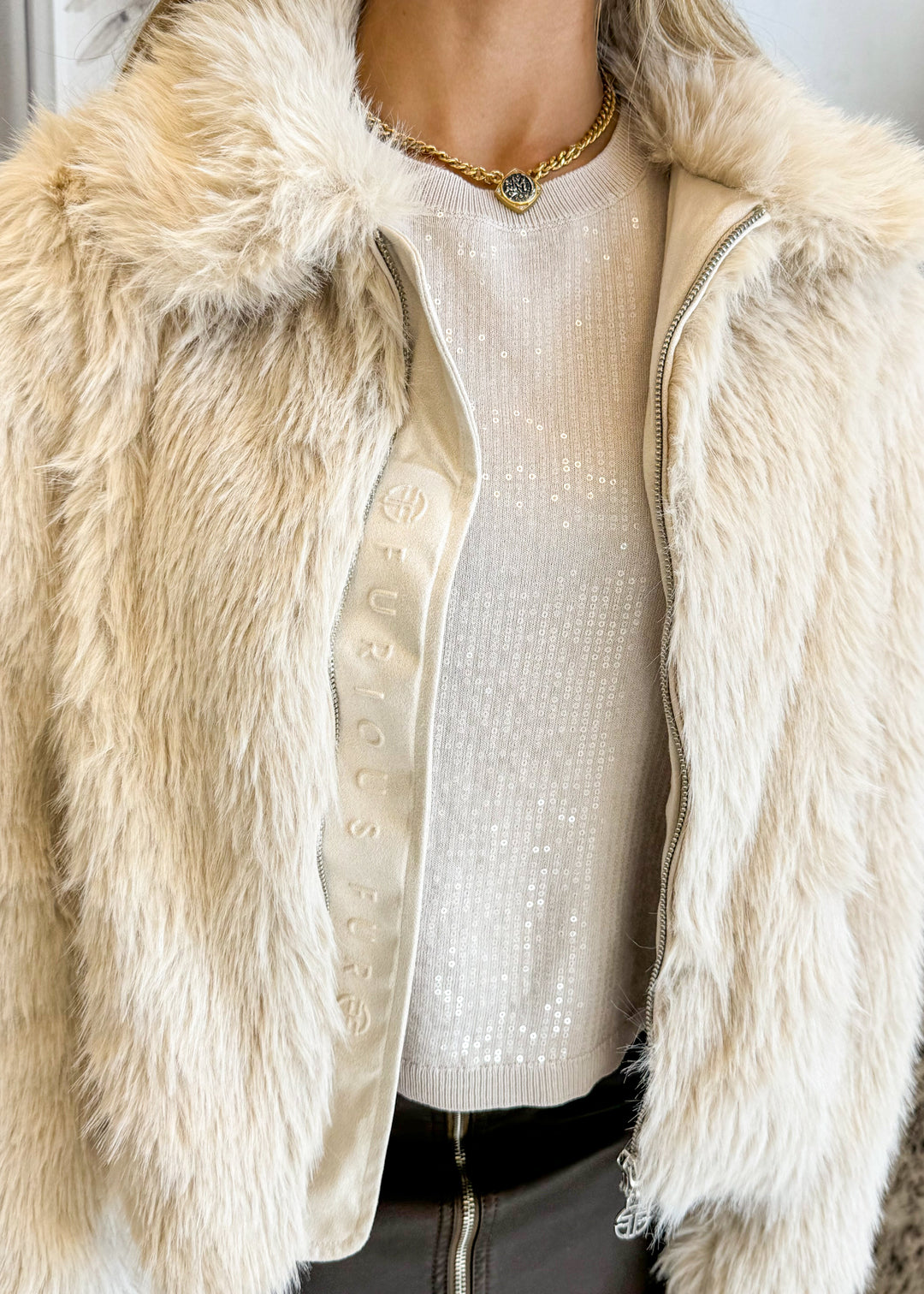 Close-up of a person wearing a beige fur coat over a white sequin top.