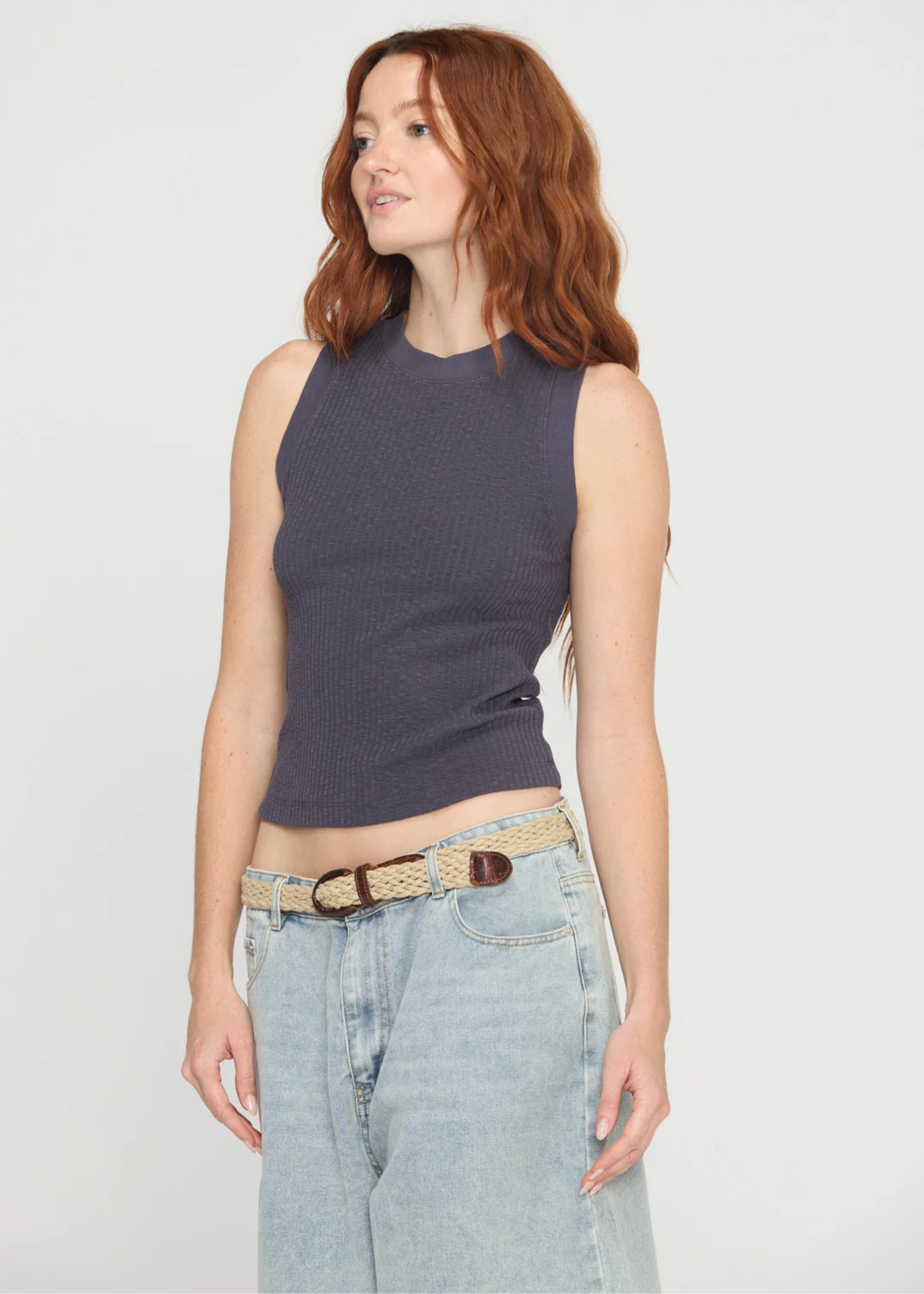 Woman wearing a charcoal grey tank top with a crew neck and a racerback along with denim bottoms and a belt