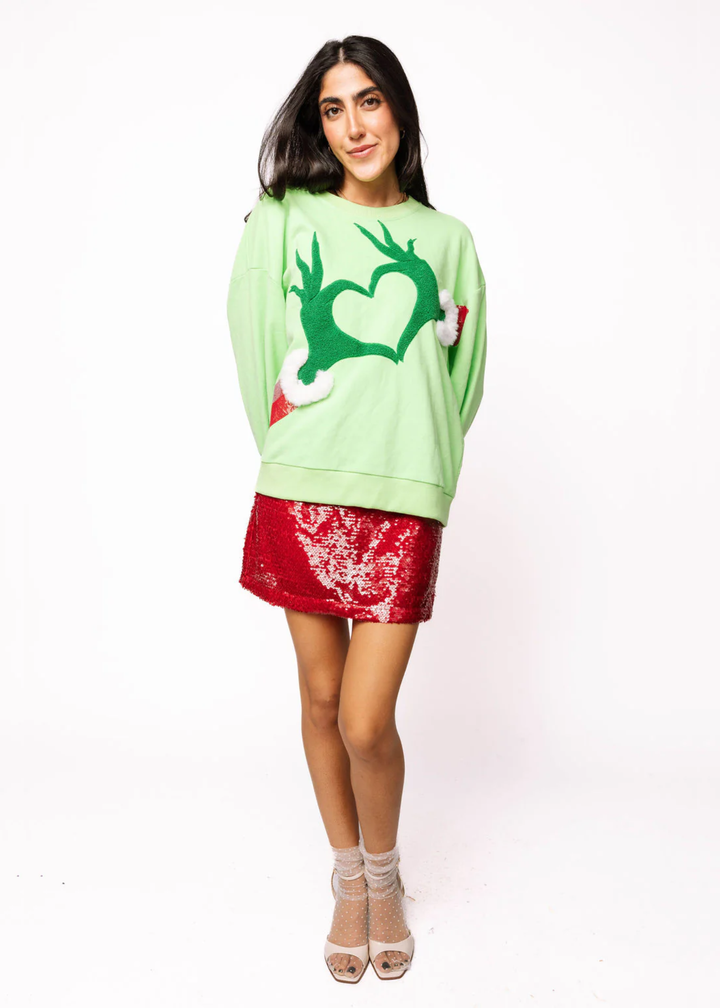Woman wearing a green sweatshirt with grinch hands in a heart shape
