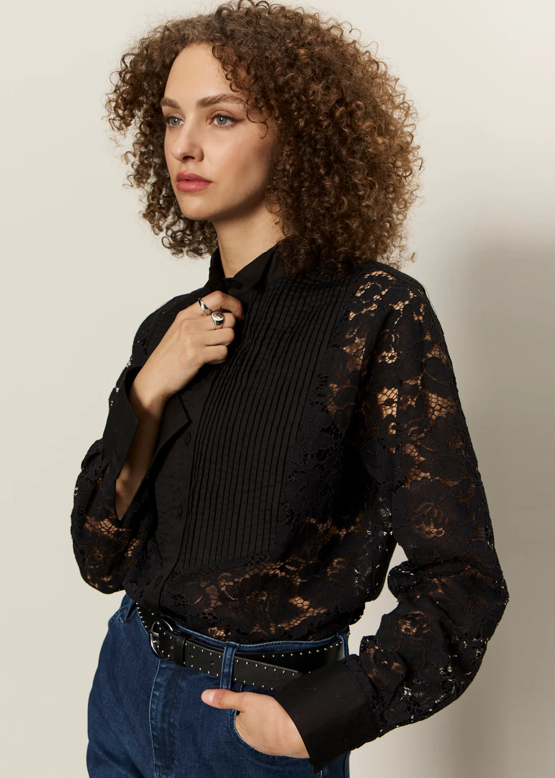 Woman wearing a black button down shirt with lace sleeves and back with jeans against a white background