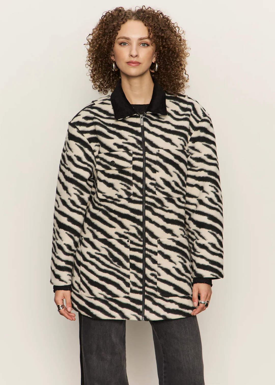 Woman wearing a white and black zebra print barn jacket with black washed jeans against a white background